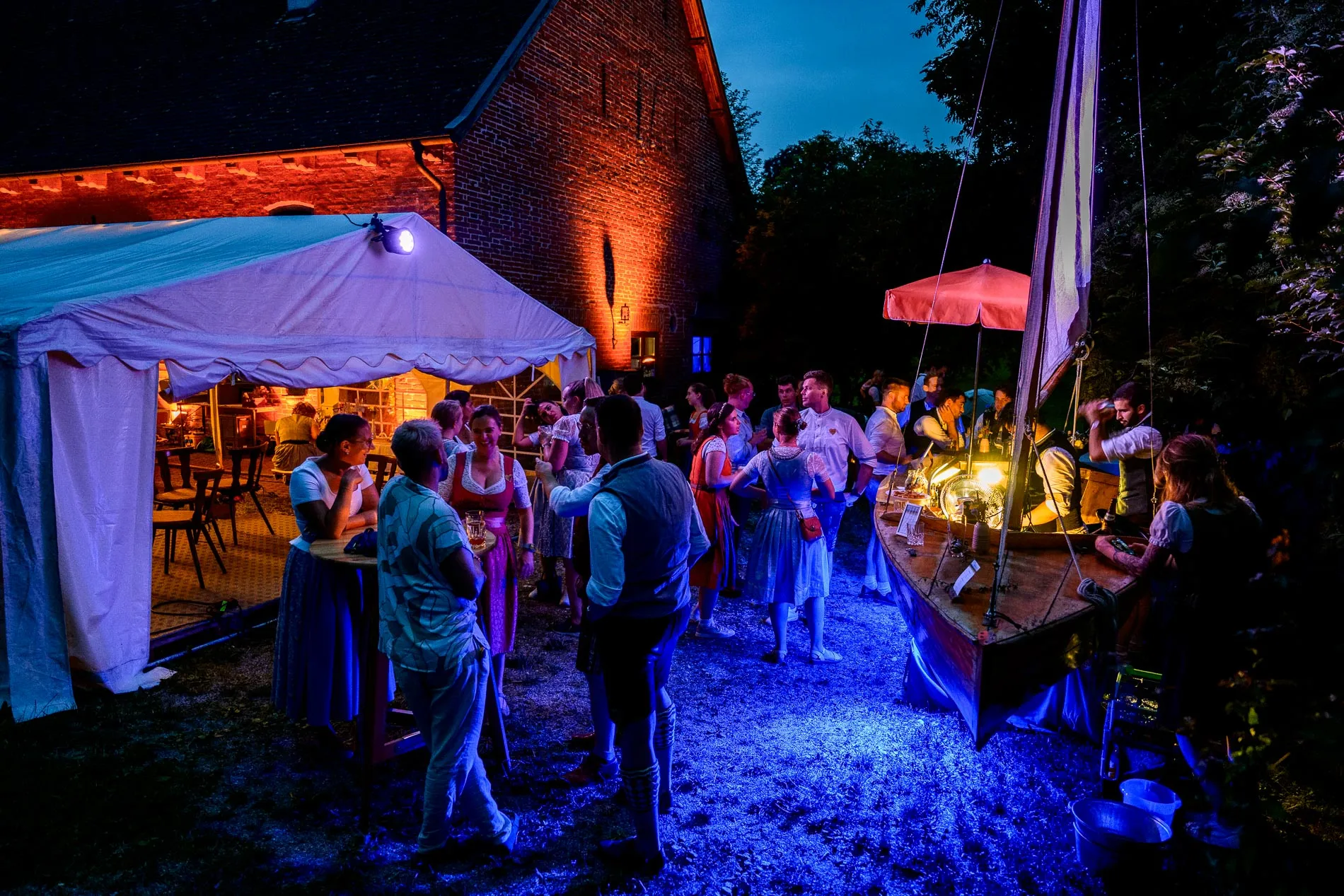 Hochzeitsfeier in Beuern bei Türkenfeld, stimmungsvolle Abendbeleuchtung, Gäste im Festzelt und am Segelbootbar.