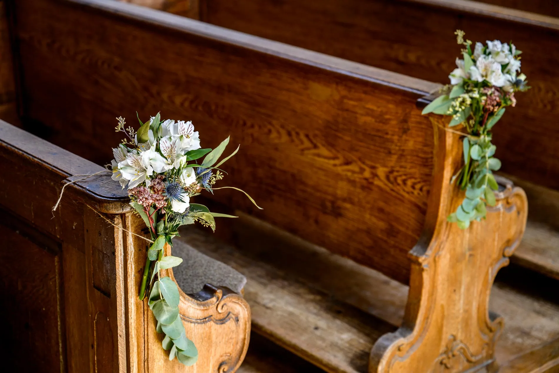 Blumenarrangement an Kirchenbank bei Hochzeit in St. Alban, Diessen am Ammersee. Romantische Details der Trauung.
